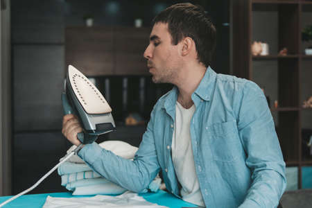 A young man irons his clean clothes after washing at home against the background of the home interior. men's domestic workの写真素材