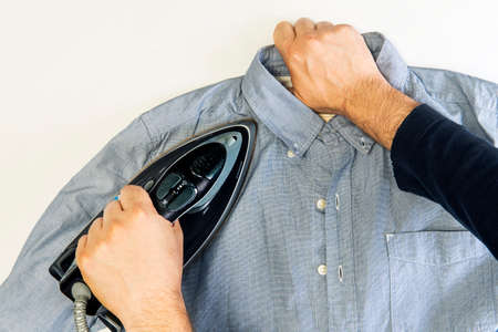 mens hands with an iron look at a blue shirt on white background. top viewの写真素材