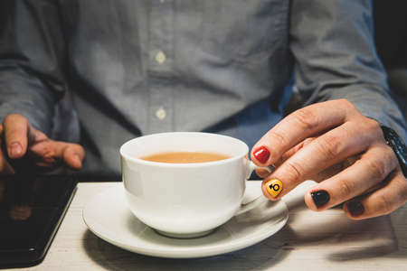 Hands of man holding cup of tea and uses a smartphone on the wood table. A man with painted nails....