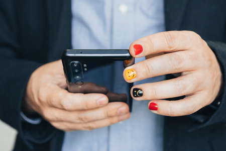 Close up of casual business man using mobile smart phone, reading business news update and marketing report via mobile app. Man with painted nails. Design of male nails. men manicure.の写真素材
