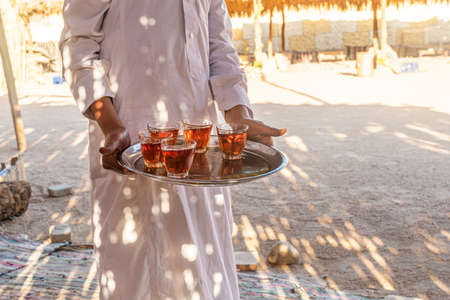 A tray with mugs of traditional Egyptian tea in the waiter's hand. Bedouin welcome a cup of tea with almonds, Sinai.の写真素材