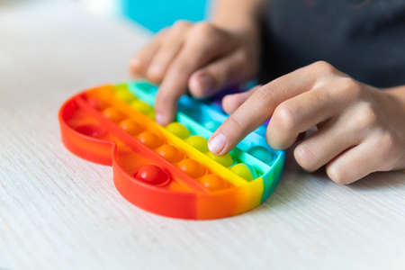 colorful antistress sensory toy fidget push pop it in kid's hands. The girl presses her finger on the rubber toy pop it on the table.の写真素材