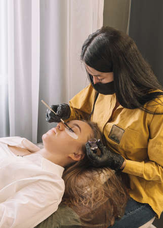 A girl in a beauty salon on the procedure of coloring her eyelashes. Care for eyebrows and...