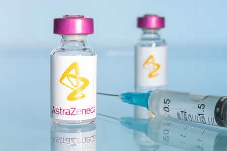 A vaccination syringe and a glass ampoule with a clear liquid on a blue background with the logo of a pharmaceutical company astrazeneca. March 15, 2021. Barnaul, Russia.のeditorial素材