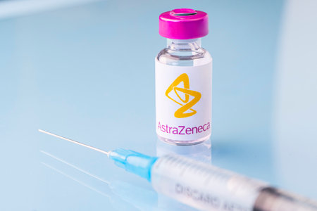 A vaccination syringe and a glass ampoule with a clear liquid on a blue background with the logo of a pharmaceutical company astrazeneca. March 15, 2021. Barnaul, Russia.のeditorial素材