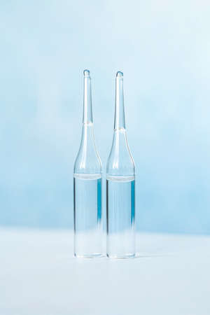 Glass vials with vaccine liquid on a blue background. The concept of medicine, vaccination and injection.の写真素材