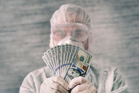 A doctor in a protective uniform holds cash bills in his hands. Payment for the doctor's work. The...