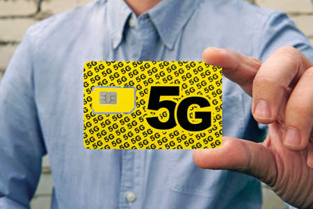 A man holds a yellow SIM card with the inscription 5G for mobile phone in his hand. Replacing the...