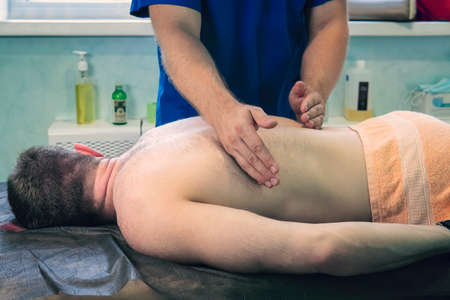 Sports massage - Masseuse using massage oil. male patient at an appointment with a physiotherapist for a massage procedure.の写真素材