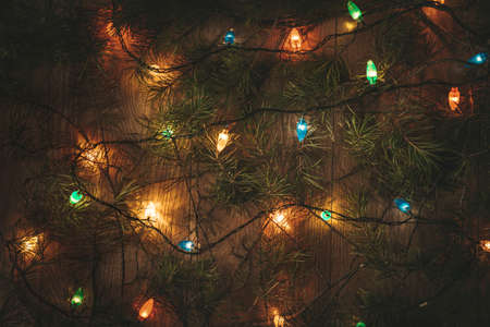 Christmas colorful lights and the green branches of the Christmas tree on wooden tableの写真素材