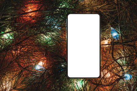 Smartphone surrounded by Christmas tree and accessories. Smartphone surrounded by fir branches. Blank screen for design or text. Christmas decorations and technology concept.の写真素材