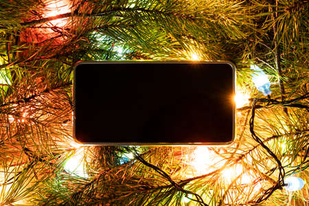 Smartphone surrounded by fir branches. Blank screen for design or text. Christmas decorations and technology concept.の写真素材