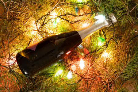 a bottle of green champagne wrapped in a glowing garland like a Christmas tree. New year concept on natural background. copy space for bottle designの写真素材