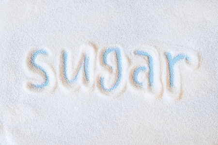 Word sugar hand lettering on placer of refined white sugar. Beet sugar crystals granules on a blue backgroundの写真素材