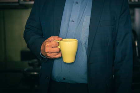 green mug in the hands of a man in a blue jacket. An employee on a coffee break. A break in work. Businessman and coffee.の写真素材