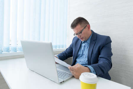 A young desperate businessman in his office looking paper documents. office worker is intensely...