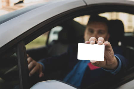 Young man with sitting in car showing an empty white card. Driver has got driving license and is very happy. Parking pass or entrance.の写真素材