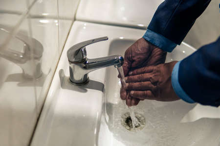 Afro American man is washing his hands in bathroom. Hygienic procedures. Cleaning your hands of bacteria and viruses.の写真素材