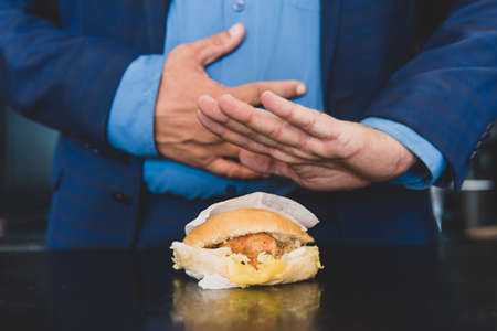 Businessman having stomachache because of eating junk food. A man who has eaten too much refuses a burger. Indigestion of the intestines from poor-quality food. Diarrhea conceptの写真素材