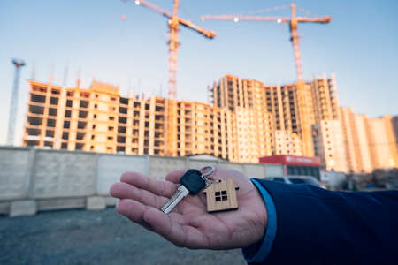 House purchase and real estate concept. Key with house keychain in hand on construction site background.の写真素材