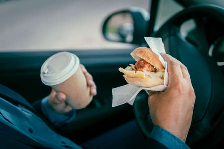 Business man having a breakfast inside the car. The driver is having lunch. fast food, junk food in the hand of a young businessman in a suit.の写真素材