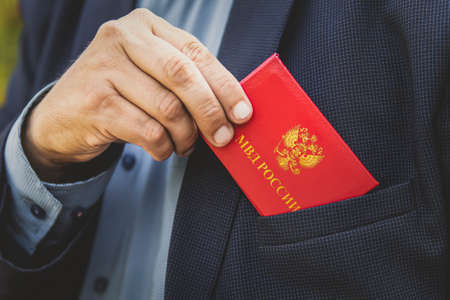 Man With Id Card. Man in a blue suit shows red ID card or a pass. An important untouchable employee of the ministry is driving a car. Interior Ministry of Russia inscription on the red document.の写真素材