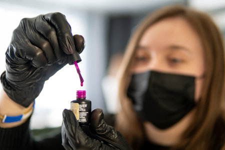 a woman manicurist opens a bottle of pink nail polish that would paint the nails of clients. a...