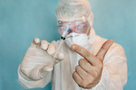 a doctor in a protective suit holds a syringe containing the covid 19 coronavirus vaccineの写真素材