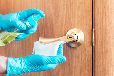 woman disinfects the door handle with a disinfectant liquid. spraying the door handle and wiping with a cloth. Disinfection of premises.の写真素材