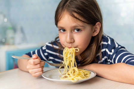 Kids eat pasta. Healthy lunch for children. Toddler kid eating spaghetti Bolognese in a blue kitchen at home. Preschooler child try noodles for dinner. Food for family.の写真素材