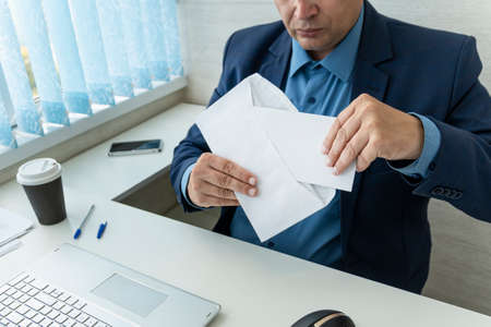 Crop close up of male employee or CEO sit at table open envelope with postal letter or mail. Caucasian businessman consider receive post paper correspondence or document message at workplace.の写真素材
