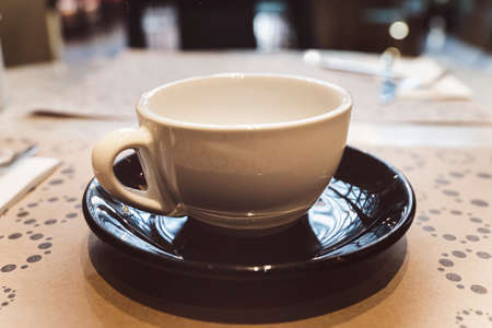 a white mug on a black saucer is on the table in the restaurant.の写真素材