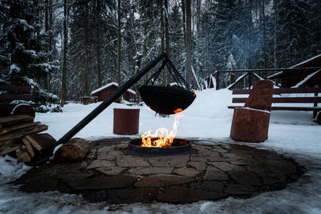 Over the fire hangs a pot in which to cook food. On a hook on a tripod, steam comes out of the pan. Winter Camping outdoor cookingの写真素材