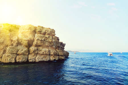 A rocky shore on the Red Sea in Egypt. Bright sun rays behind a high mountain. Beautiful seascape...