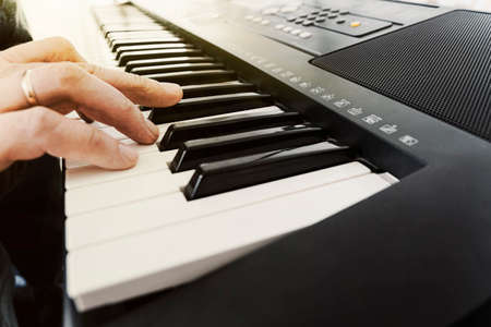 Male hands playing electric synthesizer Digital Piano, fingers pushing keys. Musician man piano player accompanist on black and white keyboards at a concert stage show. electro synthesizer and handの写真素材