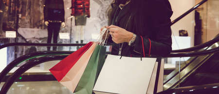 Horizontal shot of crop woman in leather black jacket holding many shopping bags and moving down on...