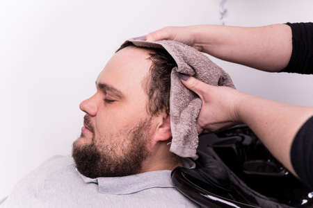 A young bearded man of Caucasian appearance at a reception at a barber shop. The process of cutting...