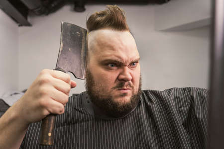 Barbershop background with brutal shaving with machete of bearded man. stern manly man shaves his head on his own looking in the mirror.の写真素材