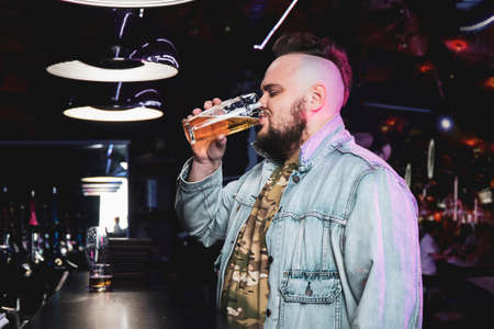 Man drinking beer. Side view of handsome young man drinking beer while sitting at the bar counter....