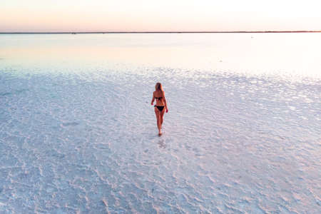a girl walks on a salty texture. girl in a black swimsuit on the background of the salty lake. Woman...
