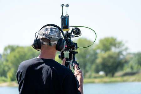 Black camera with a microphone in hand on a blurry light green background. The video operator makes...