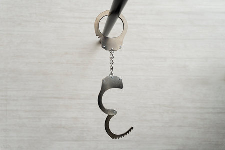 Handcuffs hanging on black pipe near white wall indoors. concept of arrest of unfreedom or sexual...