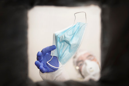 A medical technician throws away a face mask. Hand in medical gloves throwing out discarded, used...