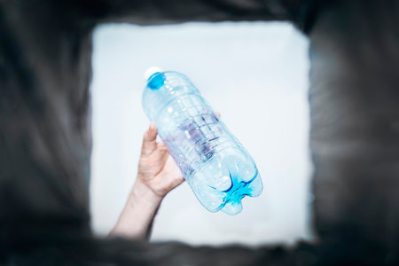 man throws empty plastic bottle into a trash can. Bottom view from the trash can. The problem of...