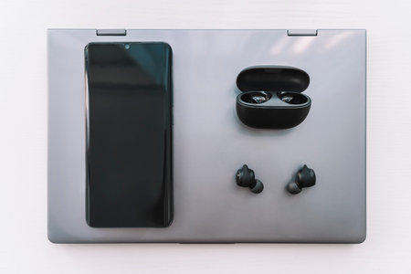 A Laptop computer, Headphones and a Smartphone on a wooden Desktop.