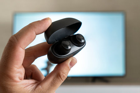 wireless headphones in the hands of a man on the background of a TV screen. watching TV with...