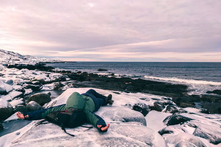 A man lies on the seashore in winter in the snow. Vacation by the Arctic Ocean. A tired traveler is...