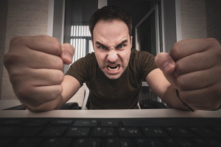 angry man swearing and cursing against information technology and his computer worries and hassles - concept of hating computers. freelancer punches the keyboard.の写真素材