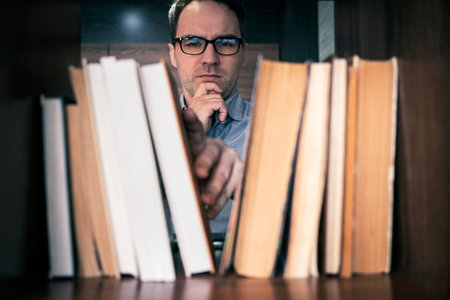 male hand choosing and picking book in public library, education research and self learning in university life conceptsの写真素材