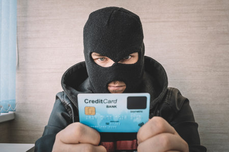 Skilled masked criminal using a stolen credit card to buy things online. A thief in a black mask...